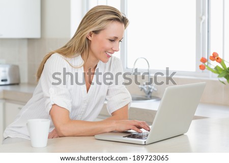 Happy woman using laptop at counter at home in the kitchen
