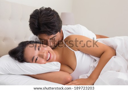 Man kissing his girlfriend on the cheek in bed at home in bedroom