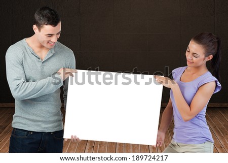 Attractive young couple showing card against dark room with floorboards
