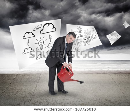 Mature businessman using watering can against sheets with graphic over sky on wall