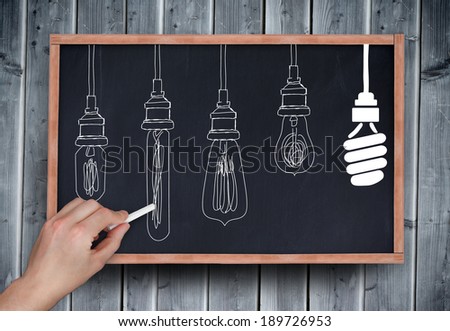 Composite image of hand drawing light bulbs with chalk on chalkboard on grey wooden planks