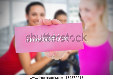 Fit blonde holding card saying innovation against exercise bike class in gym