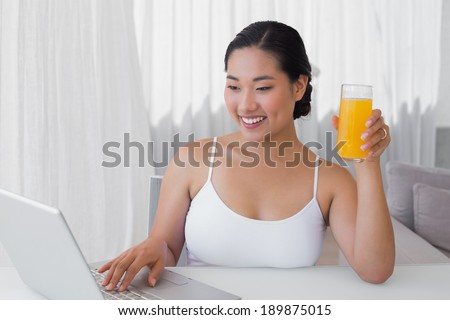 Happy woman using laptop and having orange juice at home in the living room