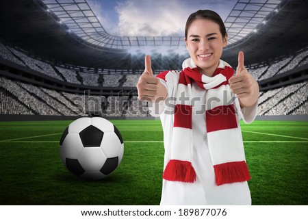 Football fan in white wearing scarf showing thumbs up against vast football stadium with fans in white