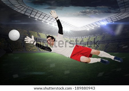 Goalkeeper in white making a save in a large football stadium with lights