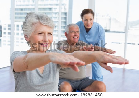 Female therapist assisting senior couple with exercises in the medical office