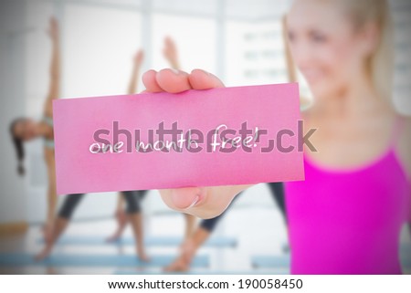 Fit blonde holding card saying one month free against fitness class in gym