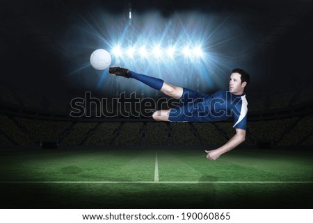 Football player in blue kicking in a football pitch under spotlights