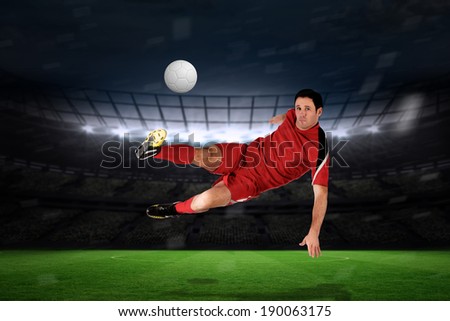 Football player in red kicking against large football stadium with fans in yellow