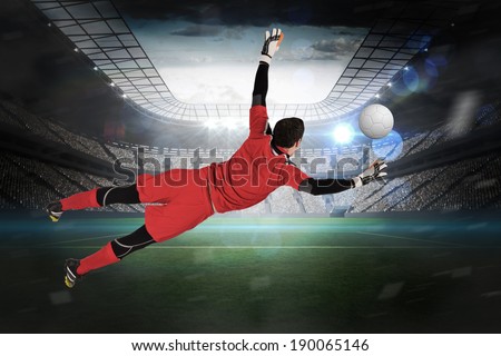 Fit goal keeper jumping up in a large football stadium with lights