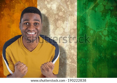 Cheering football fan in yellow jersey against ivory coast flag in grunge effect