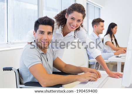 Casual businessman in wheelchair working at his desk with colleague in the office