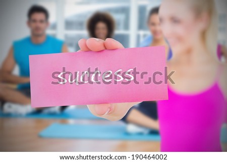 Fit blonde holding card saying success against yoga class in gym