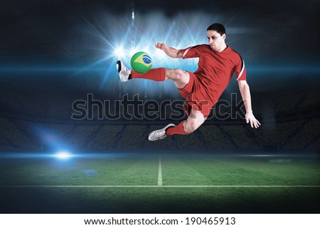 Fit football player jumping and kicking in a football pitch under spotlights