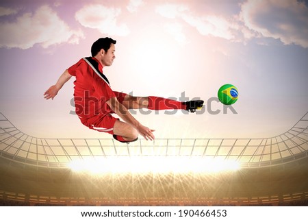 Football player in red kicking against large football stadium with spotlights under morning sky
