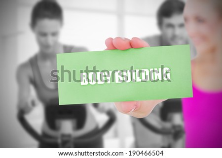 Fit blonde holding card saying body building against fitness class in gym