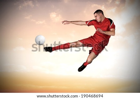 Fit football player playing and kicking against beautiful orange and blue sky
