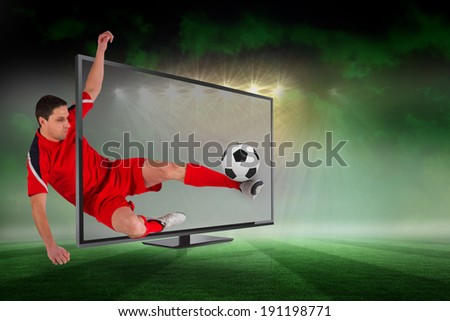 Composite image of fit football player kicking ball through tv against football pitch under green sky and spotlights