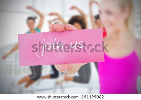 Fit blonde holding card saying join us against fitness class in gym