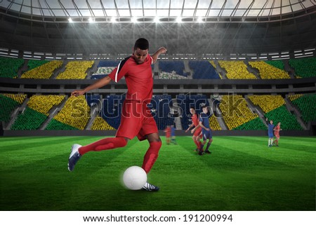 Football player in red kicking against large football stadium with brasilian fans