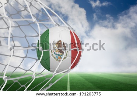 Football in mexico colours at back of net against football pitch under blue sky