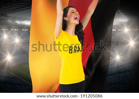 Excited football fan in brasil tshirt holding germany flag against large football stadium with fans in blue