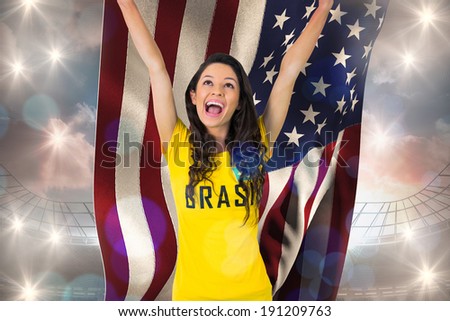 Excited football fan in brasil tshirt holding usa flag against large football stadium under cloudy blue sky