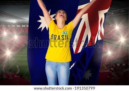Excited football fan in brasil tshirt holding australia flag against vast football stadium with fans in red
