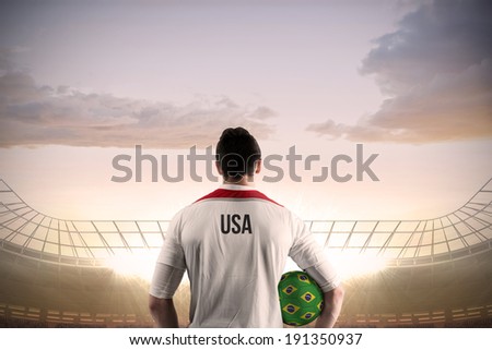 Usa football player holding ball against large football stadium under cloudy blue sky