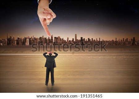 Giant hand pointing at businessman standing back to the camera with hands on head against cityscape on the horizon