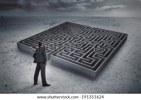 Businessman standing with hand on hip against big maze under cloudy sky