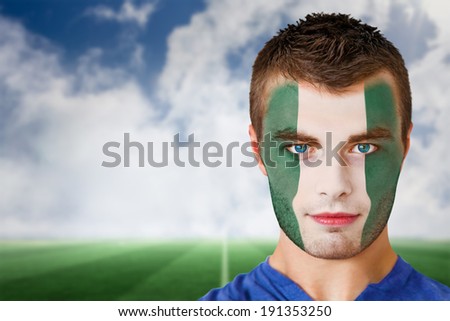 Composite image of nigeria football fan in face paint against football pitch under blue sky