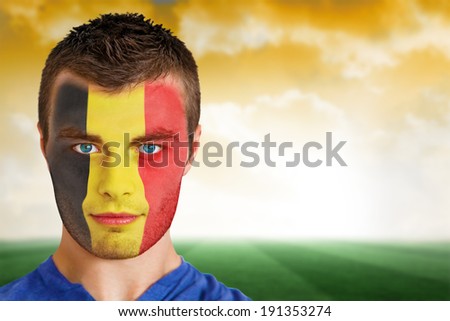 Composite image of belgium football fan in face paint against football pitch under yellow sky