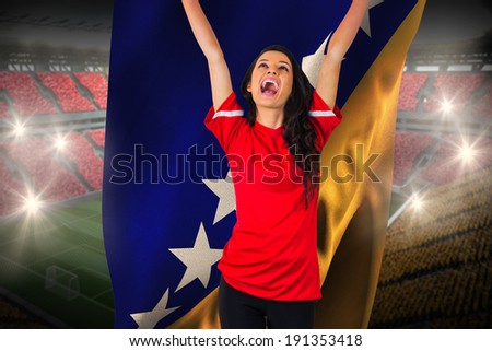 Cheering football fan in red holding bosnia flag against vast football stadium with fans in yellow and red