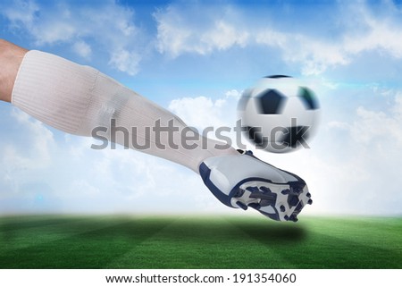 Composite image of close up of football player kicking ball against football pitch under blue sky