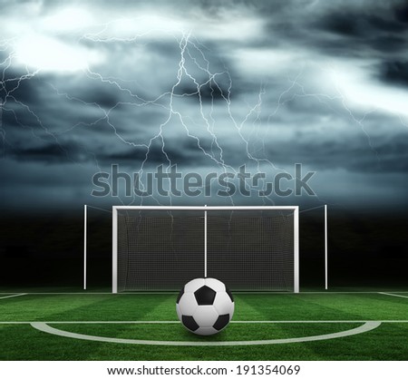 Black and white football against football pitch under stormy sky