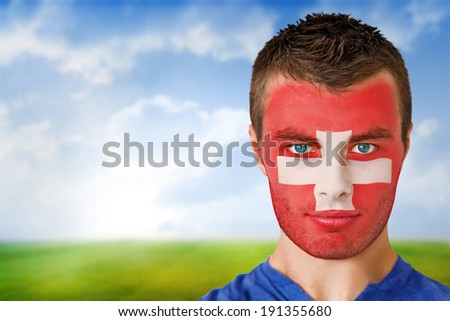 Composite image of swiss football fan in face paint against football pitch under blue sky