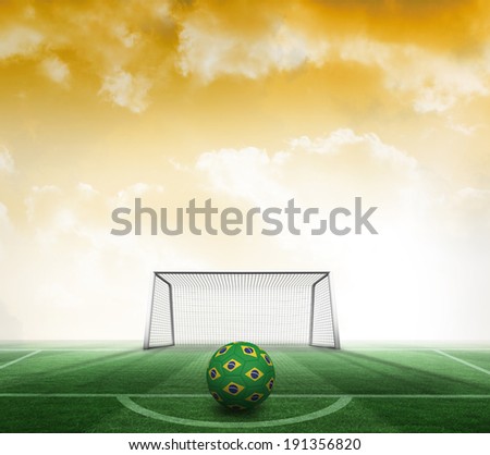 Football in brazilian colours against football pitch and goal under yellow sky