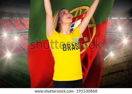 Excited football fan in brasil tshirt holding portugal flag against vast football stadium with fans in yellow and red