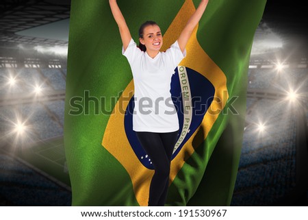 Excited football fan in white cheering holding brasil flag against large football stadium with fans in blue