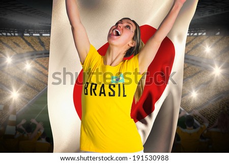 Pretty football fan in brasil t-shirt holding japan flag against vast football stadium with fans in yellow
