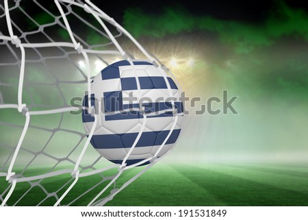 Football in greece colours at back of net against football pitch under green sky and spotlights
