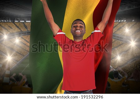 Excited handsome football fan cheering holding ghana flag against vast football stadium with fans in yellow