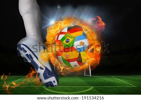 Football player kicking flaming international flag ball against football pitch and goal under spotlights