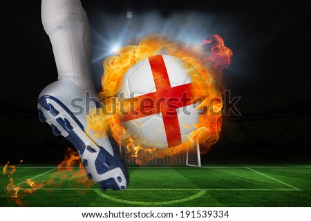 Football player kicking flaming england flag ball against football pitch and goal under spotlights