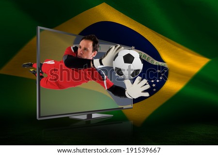 Composite image of fit goal keeper saving goal through tv against brazilian flag waving