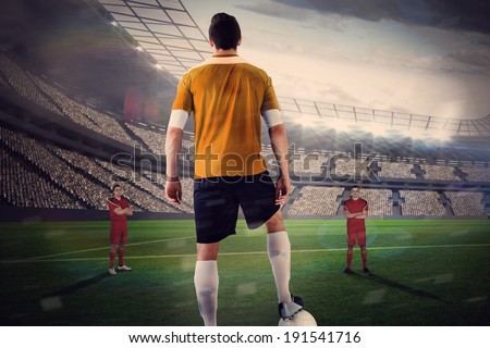 Football player in yellow with facing opposition ball against large football stadium with lights