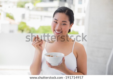 Happy woman eating bowl of cereal outside on a balcony