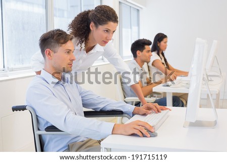 Casual businessman in wheelchair working at his desk with colleague in the office