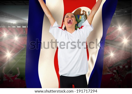 Football fan in white cheering holding costa rica flag against vast football stadium with fans in red